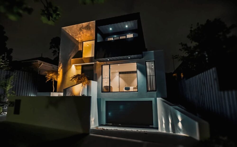 Nighttime view: modern house in McGrath Real Estate video, warmly lit, sharp angles, textured surfaces.