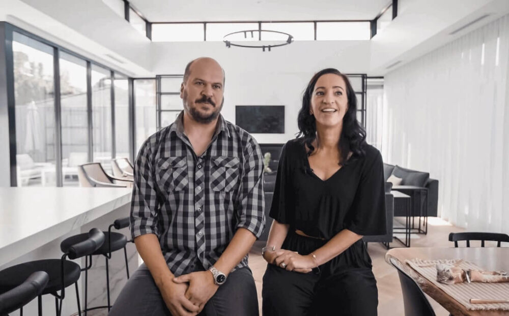 In the image from a client testimonial video for Lowe Design & Build Bayside Builders, a man and a woman are posed side by side, offering a glimpse into the elegant and well-lit space characteristic of Lowe